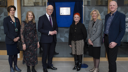 Six people stand either side of a plaque commemorating the official opening of a health, social care and community facility