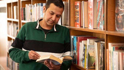 Person looking at a book and leaning against a bookshelf in Knightswood library