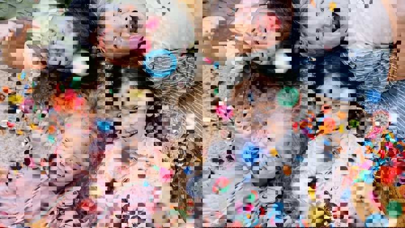 Fur young kids lying on the floor laughing with multi-coloured confetti falling on them