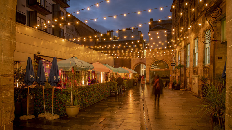 Outdoor courtyard with string lights overhead, restaurant seating under umbrellas, and warm evening glow.